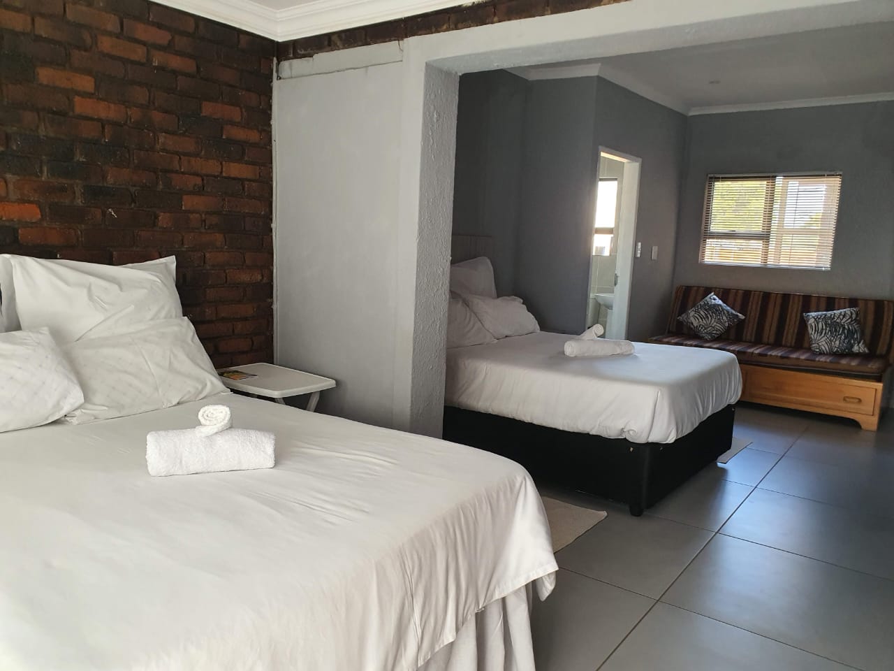 Room with two double beds and brick feature wall at Zea85 B&B